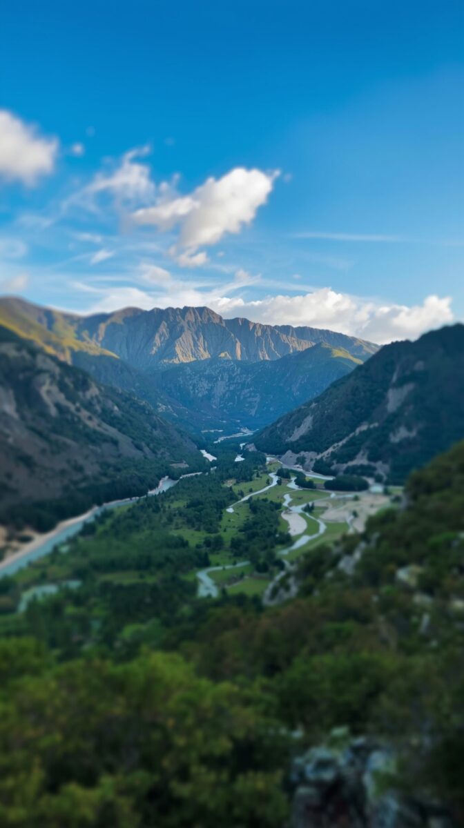Aerial view of a winding river valley between rugged mountains under a blue sky with white clouds