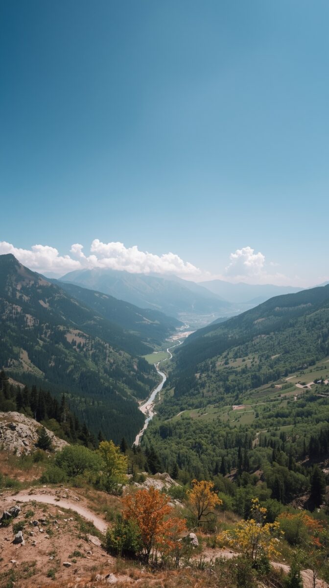 Aerial view of a lush mountain valley with a winding river, forested slopes, and blue sky with clouds