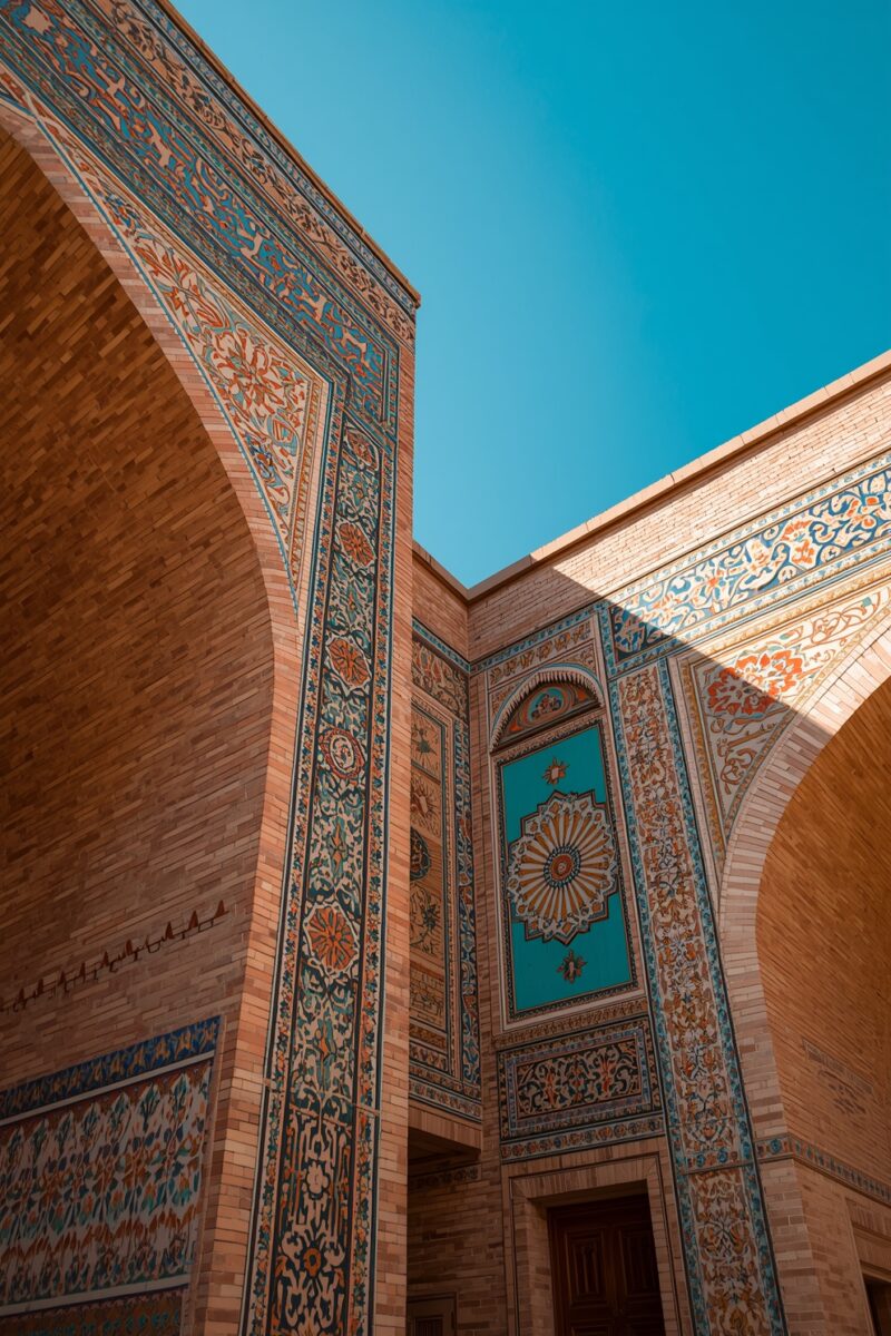 Ornate Islamic architecture with turquoise and orange tilework on brick walls with arched doorways under blue sky