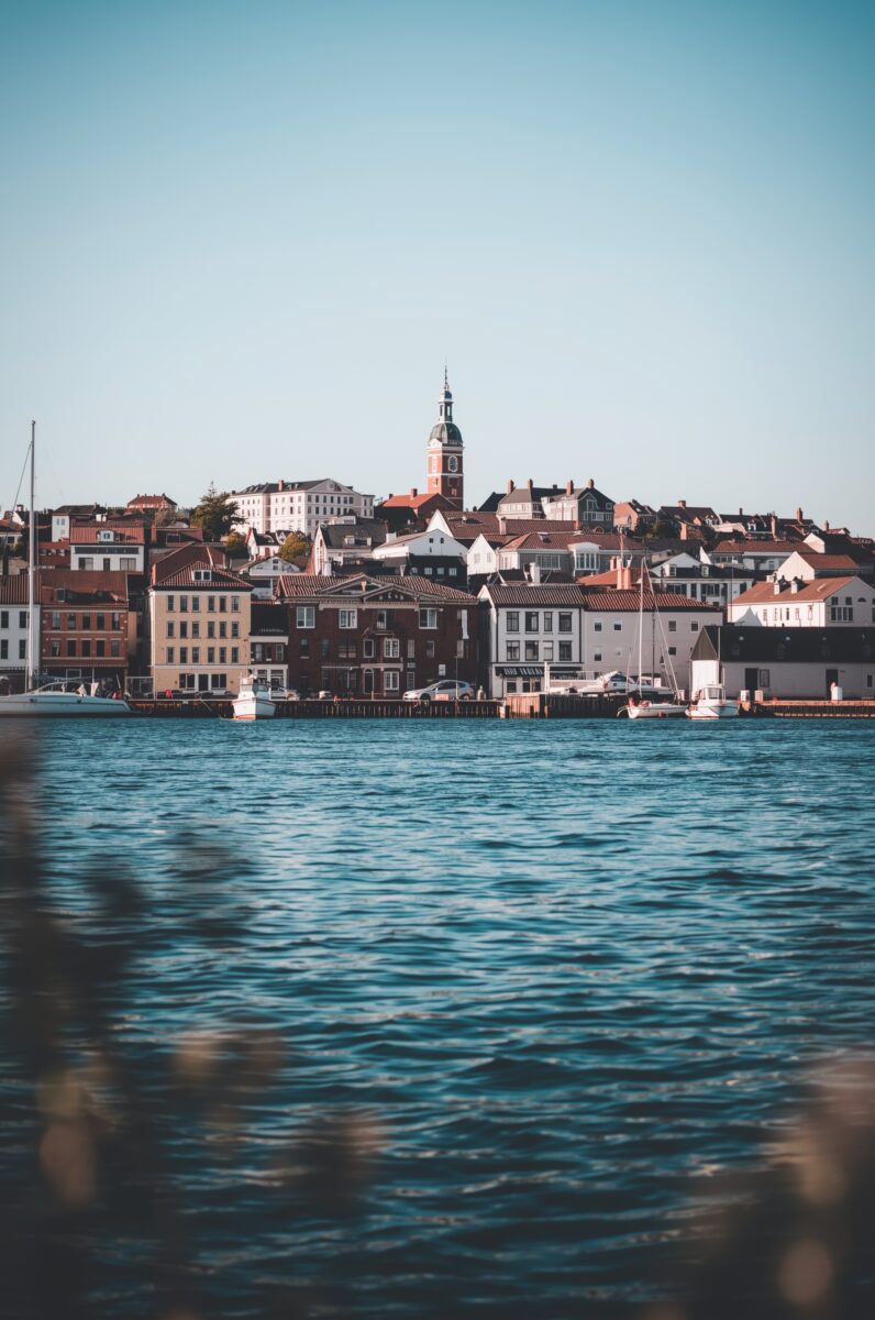 Scenic waterfront view of a Scandinavian coastal town with red-roofed buildings and a church clock tower