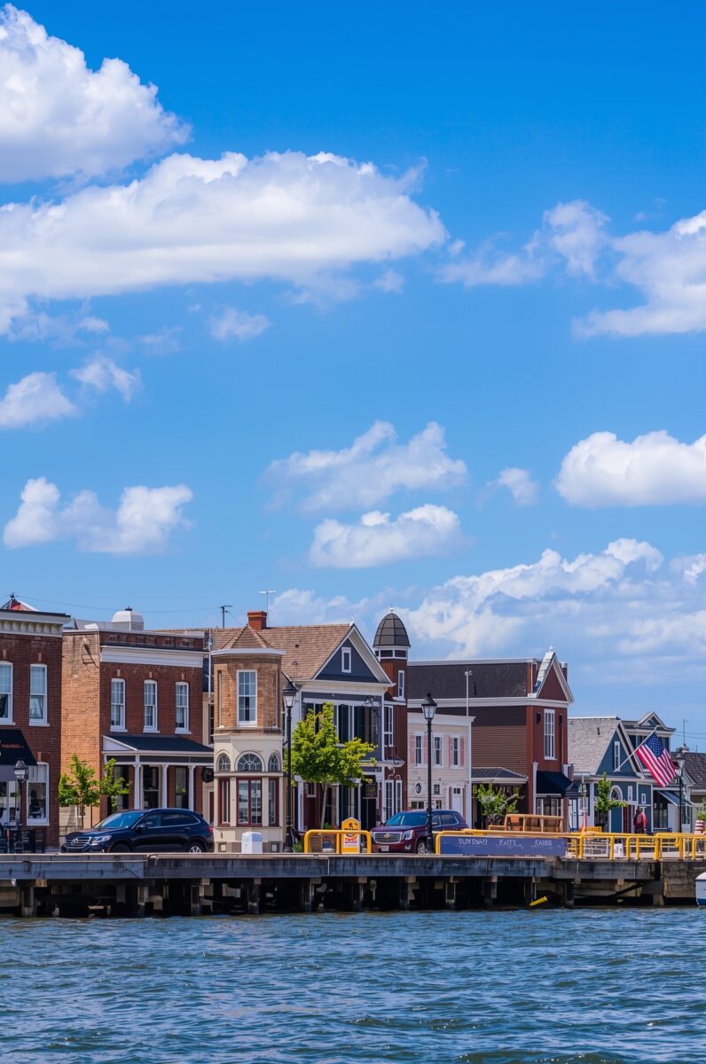 Historic waterfront town with Victorian and brick buildings lining a pier under a bright blue sky