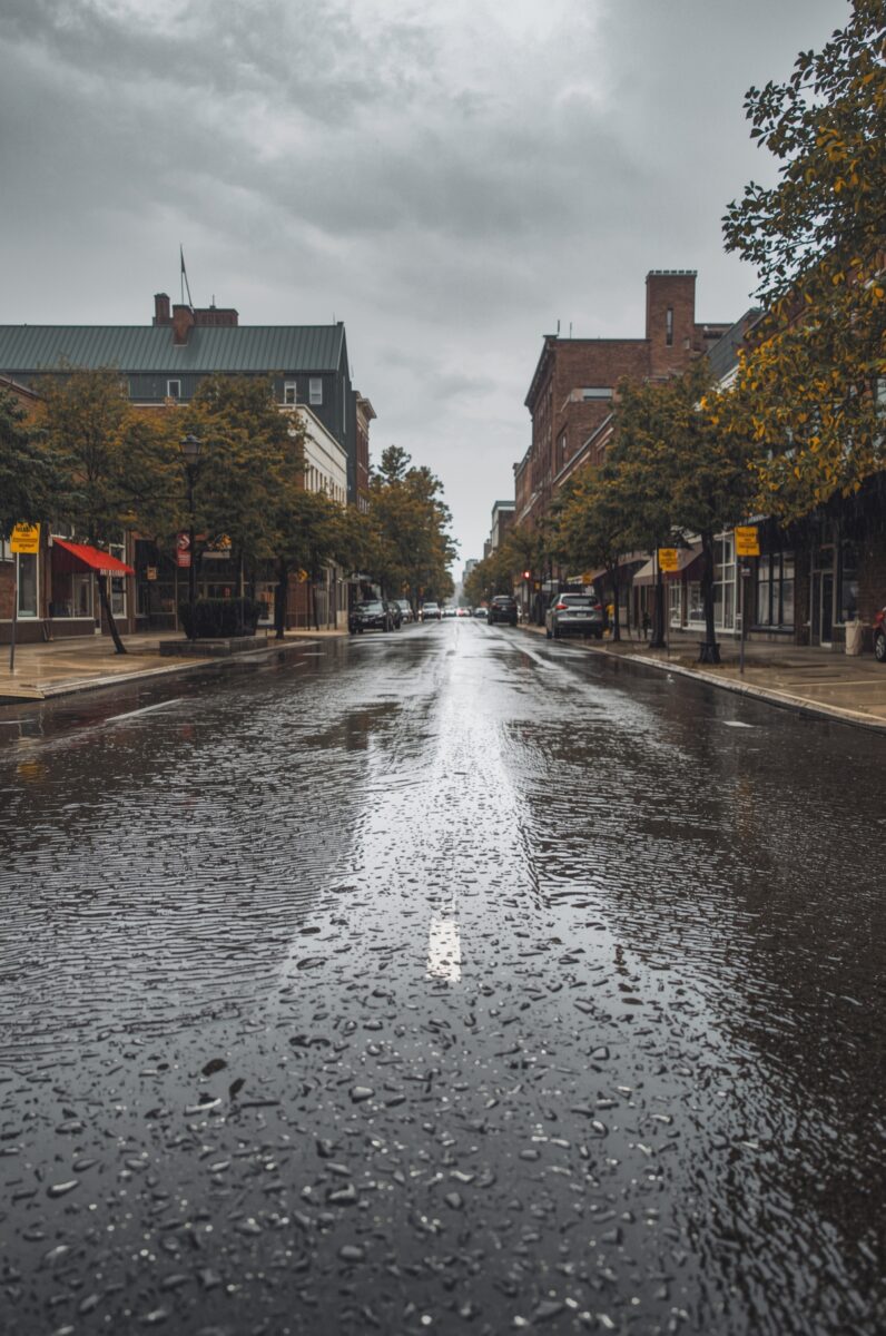 Rain-soaked empty main street lined with brick buildings, trees, and parked cars on a overcast autumn day