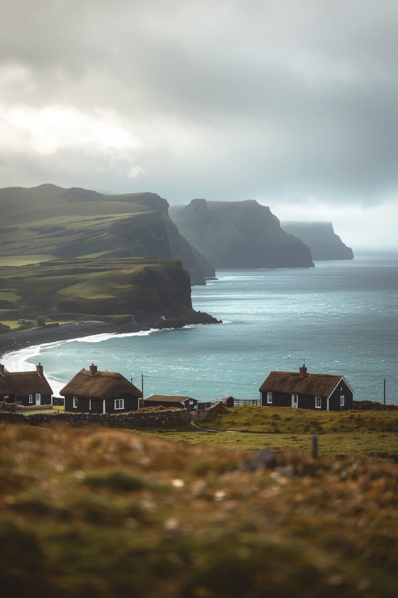 Traditional thatched cottages overlooking dramatic coastal cliffs and turquoise sea under moody overcast skies