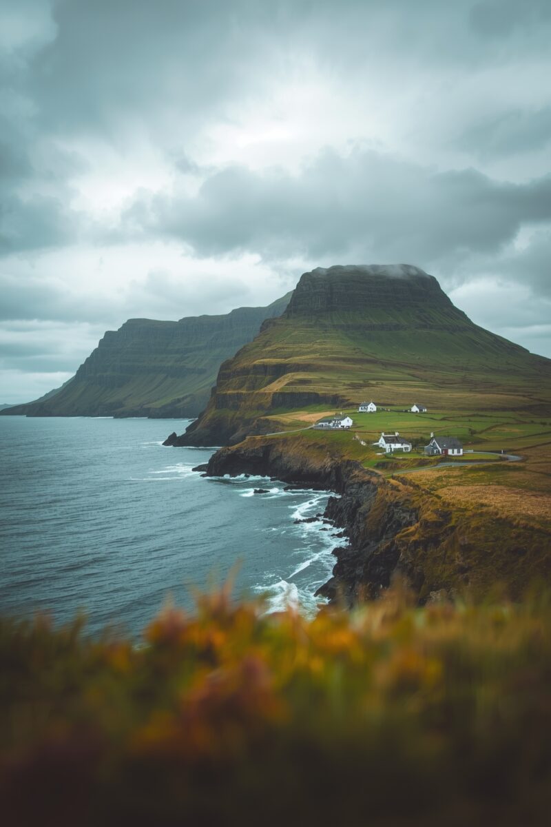 Dramatic coastal cliffs with a flat-topped green mountain, white farmhouses, and stormy seas in a remote Atlantic landscape