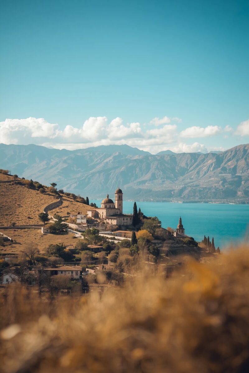 Historic domed church and bell tower on a hillside overlooking a turquoise lake with mountains in background