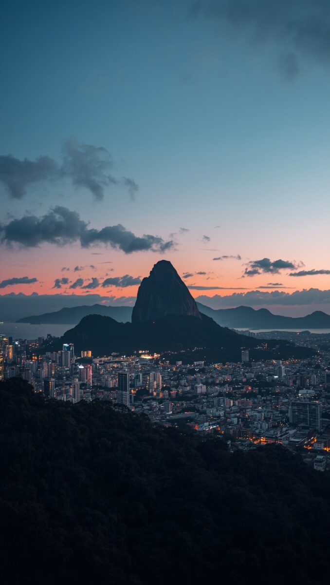 Aerial twilight view of Rio de Janeiro with Sugarloaf Mountain silhouetted against an orange and blue sunset sky