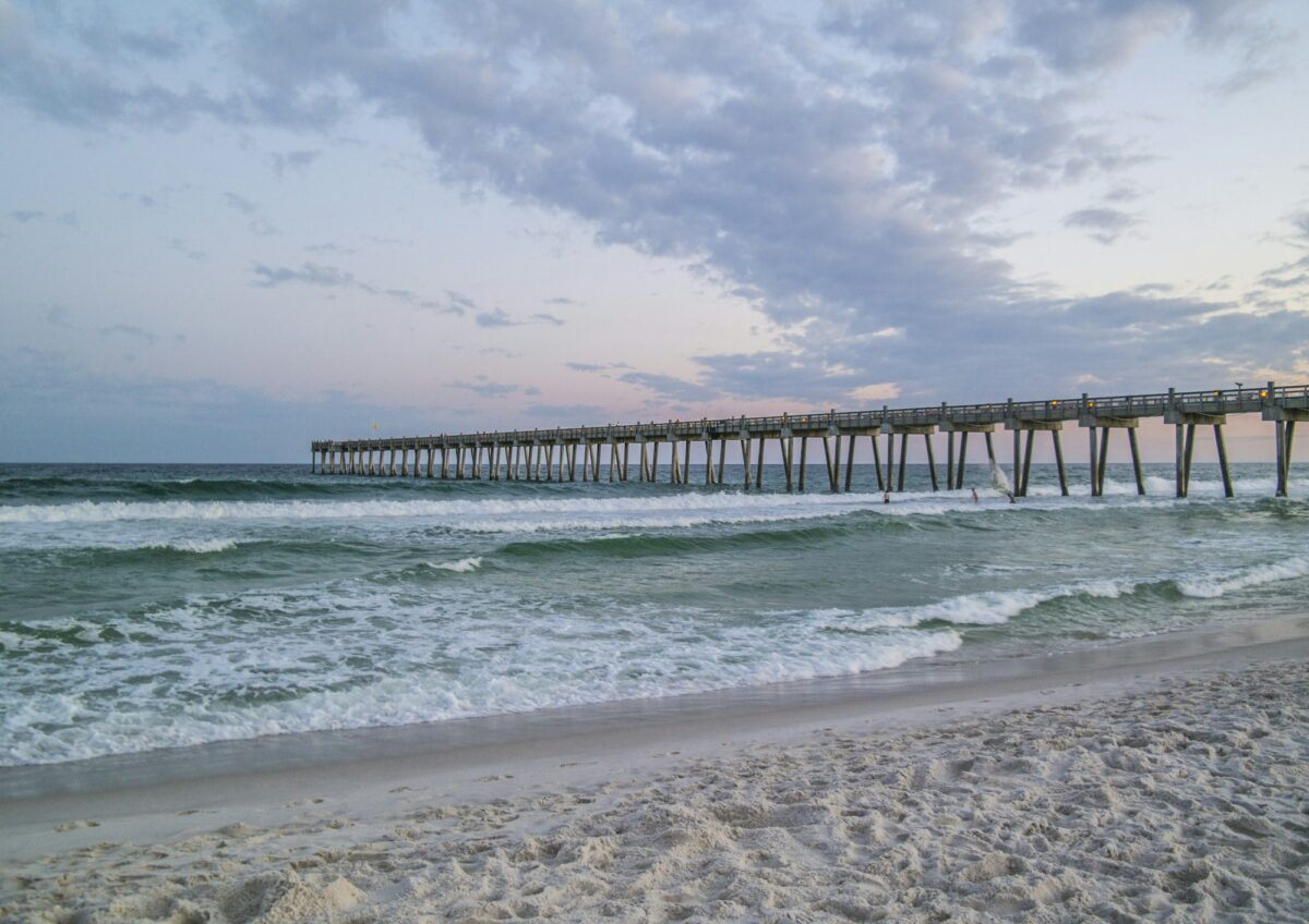 Pensacola Beach and its fishing pier under a cloudy evening sky, with white sand and rough gray-green water
