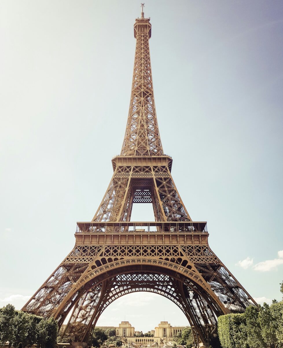 The Eiffel Tower from the Champ de Mars, its first and second floor platforms clear against a pale sky