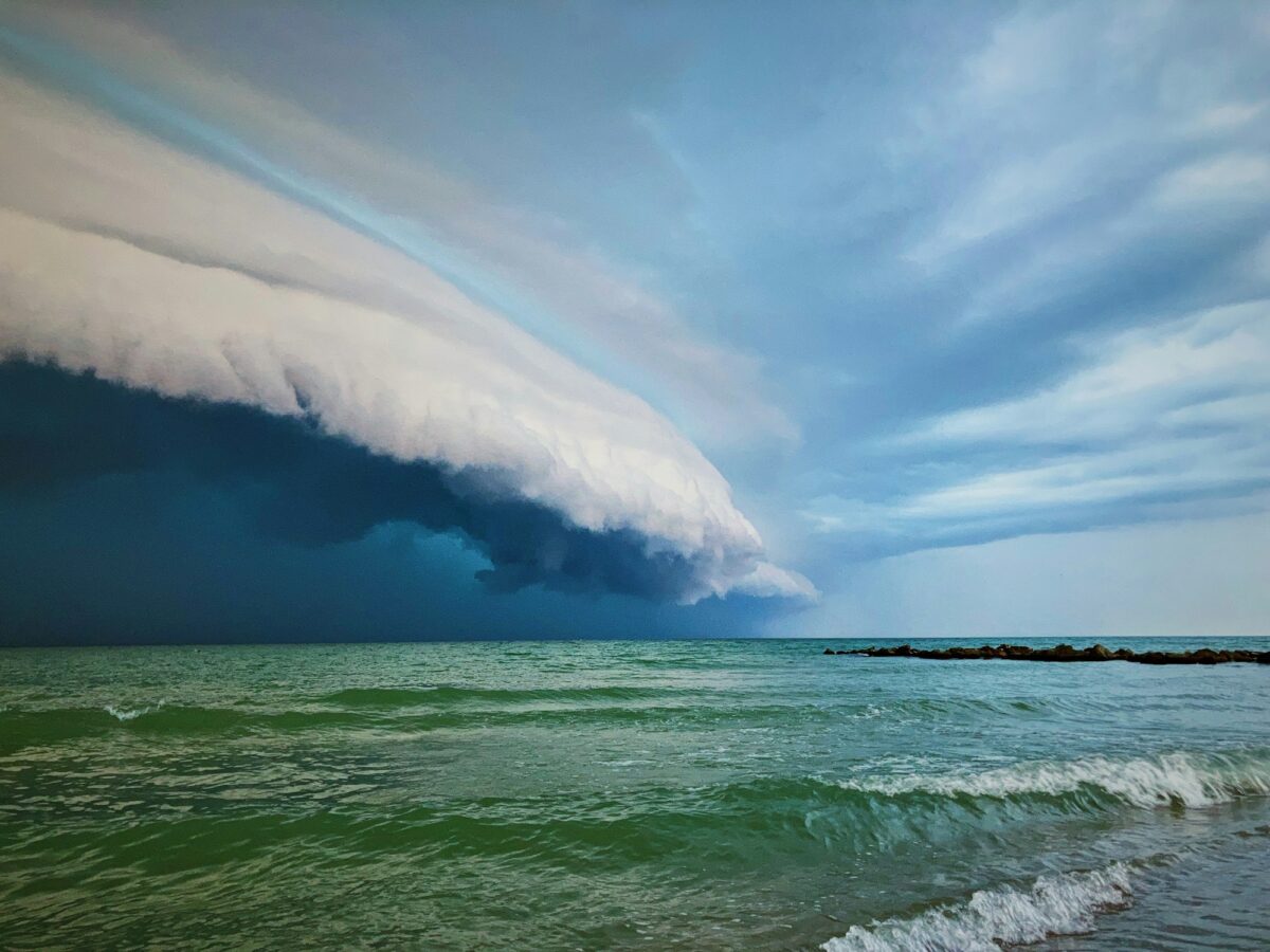 A storm front rolling in low over a green sea, waves breaking on the shore under it