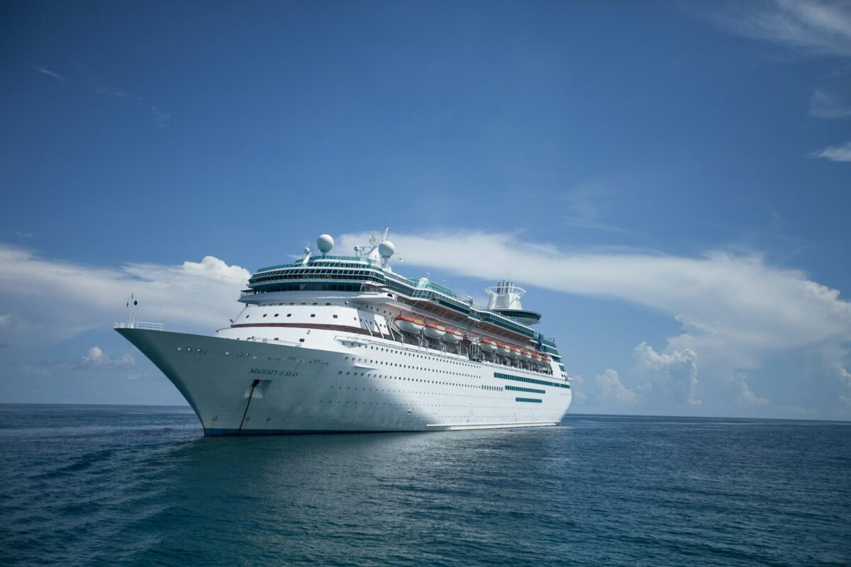 A large white cruise ship sitting at anchor in calm blue water under a few clouds