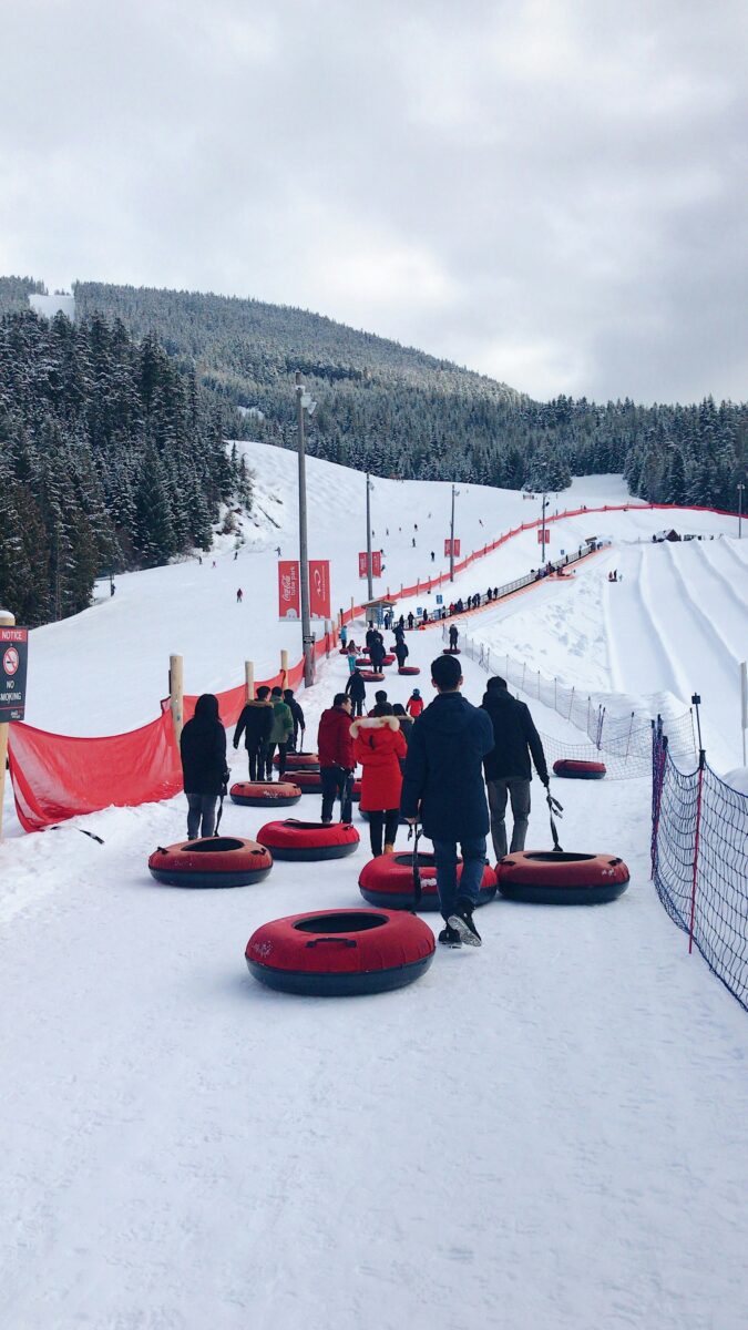 People walking up snow tubing lanes pulling red tubes at Whistler, British Columbia