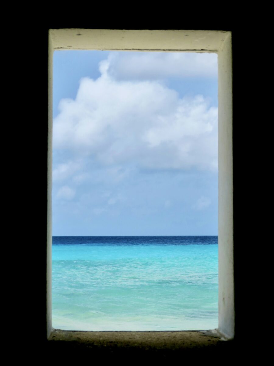 Turquoise water and a cloudy sky on Bonaire, seen through a small white window in a dark wall