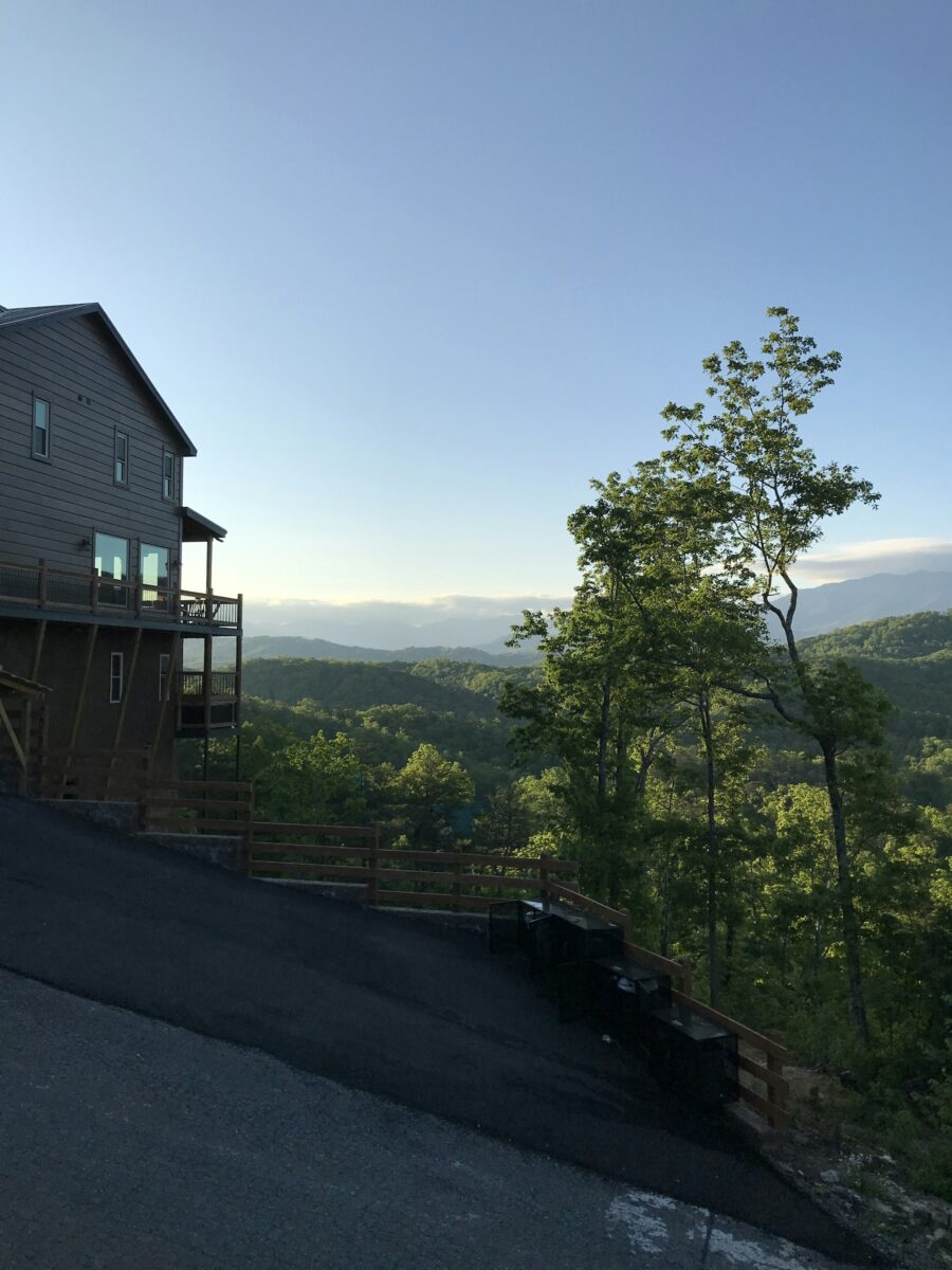 A tall house with decks on a hillside in Gatlinburg above a steep driveway, with mountain ridges behind