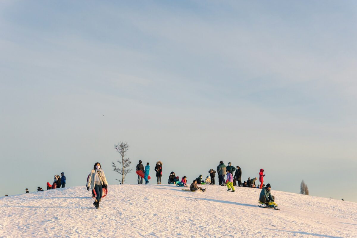 Families with sleds on the crest of a snowy hill under a pale winter sky in Richmond, British Columbia
