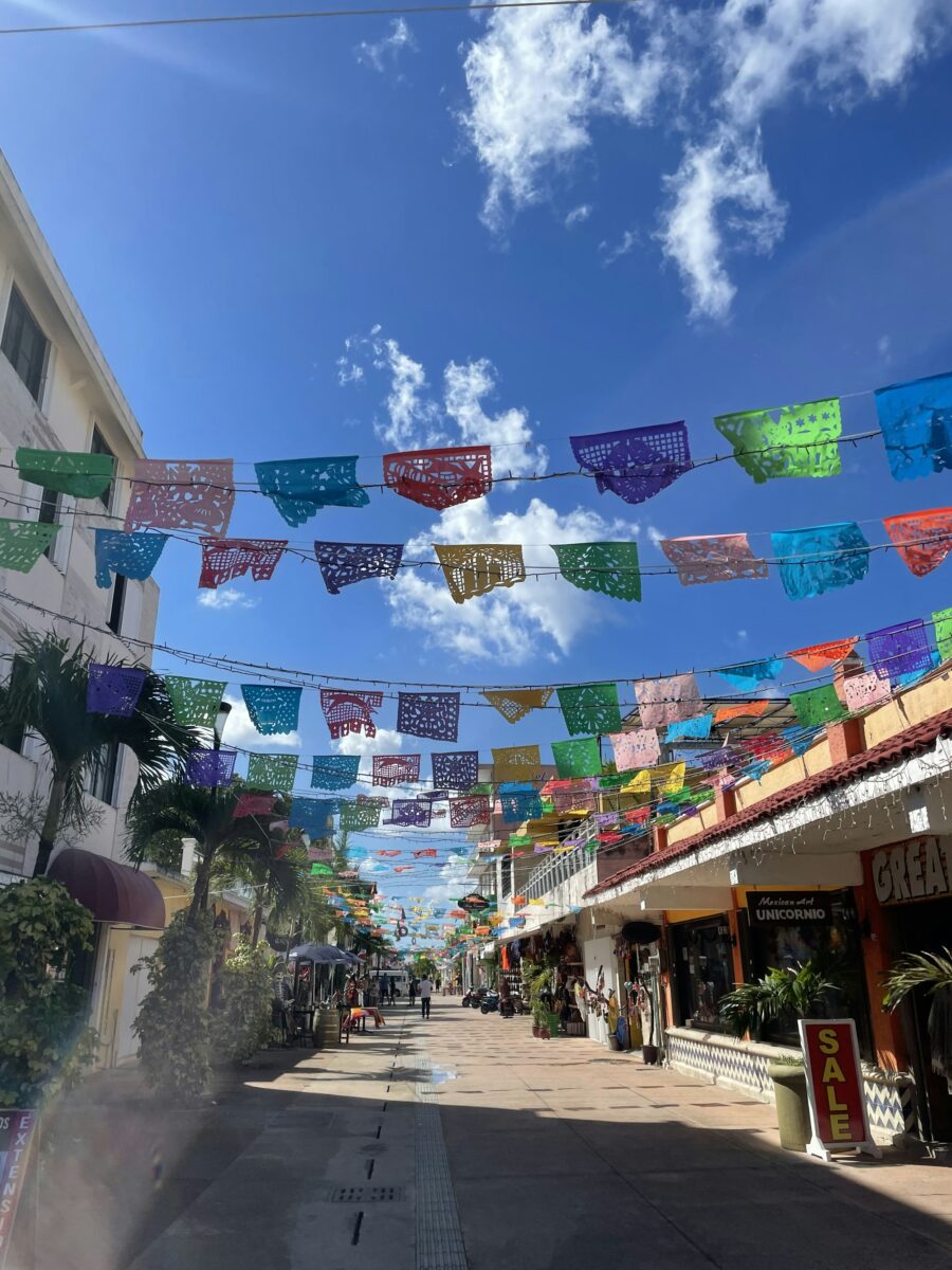 Rows of colorful cut-paper flags strung over a shopping street in Cozumel, Mexico, shops on both sides