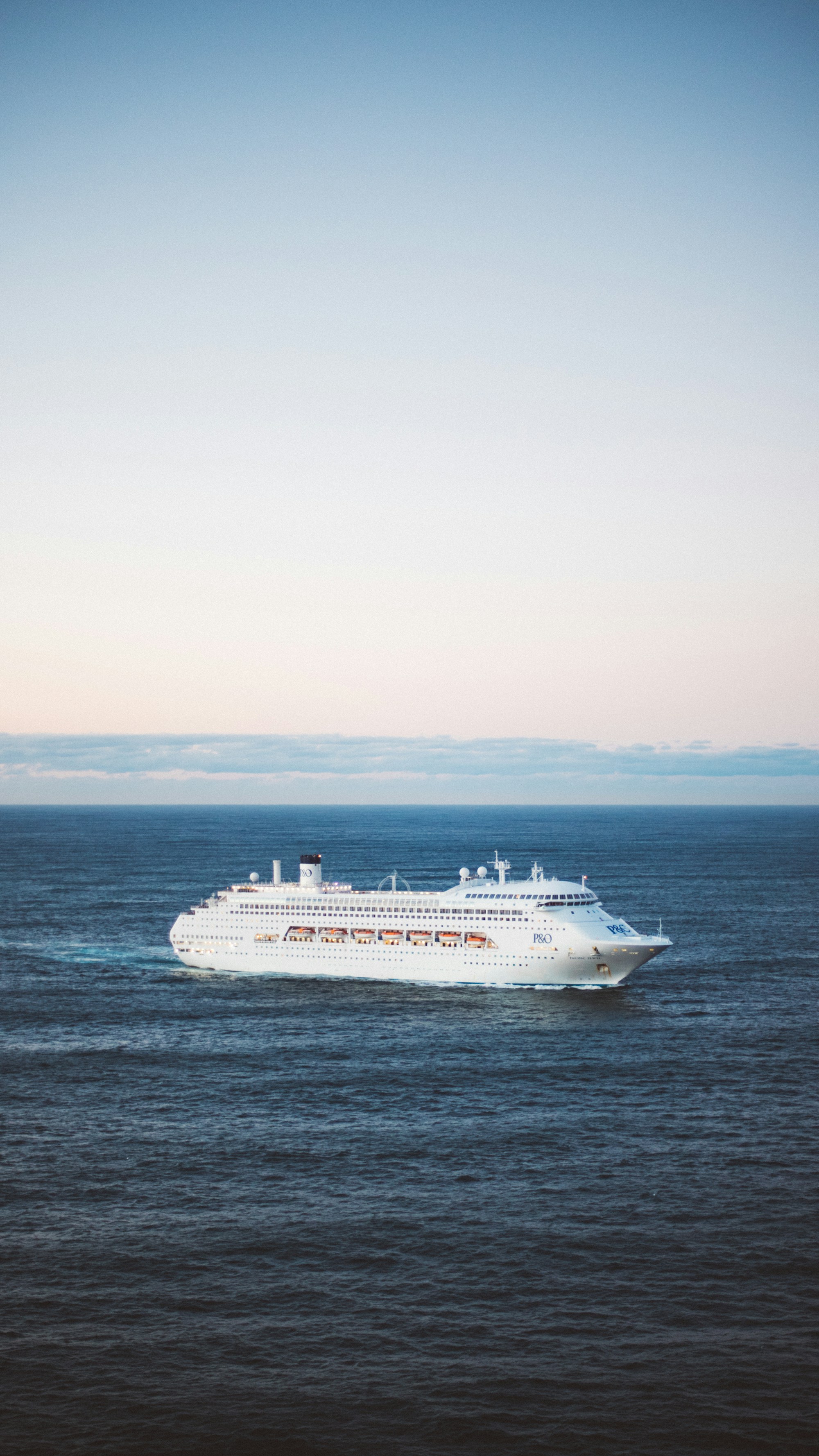 A white cruise ship at sea under a pastel sky at dusk